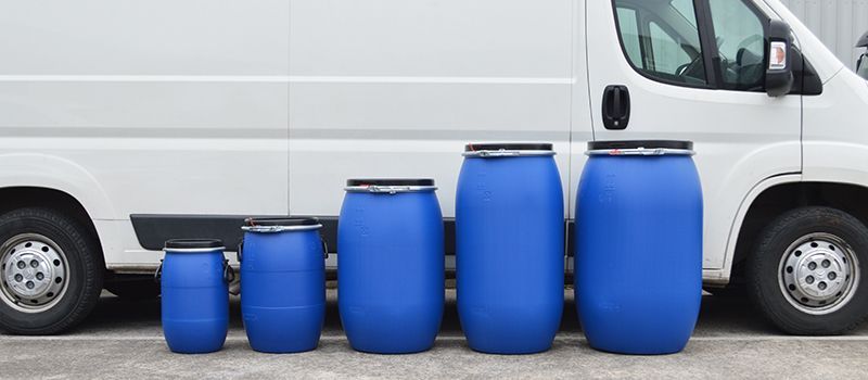 blue plastic drums in a range of sizes from small to large against a white transit van
