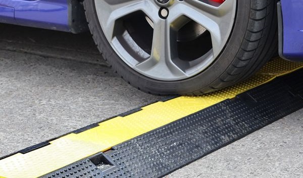 A car driving over a black and yellow heavy-duty cable protector.
